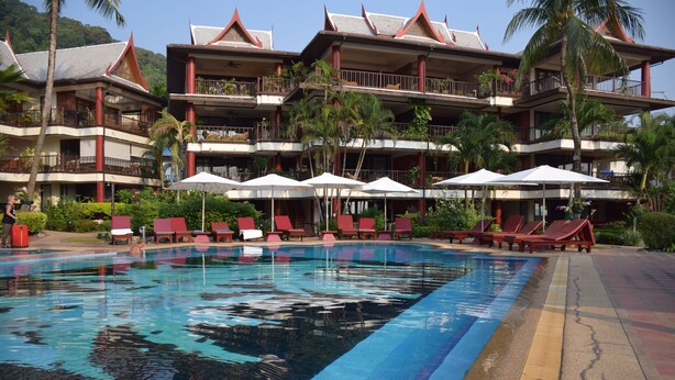 Un hôtel doté d’une grande piscine, de chaises longues rouges et d’un immeuble à plusieurs étages avec des balcons.