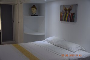 A bedroom with a bed, a shelf with a bust sculpture, and a colorful painting on the wall.