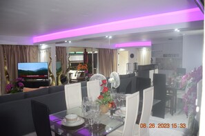 A dining area with a table set for four, a television in the background, and a modern interior design with purple lighting.