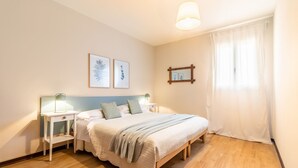 A bedroom with a bed, bedside tables, a nightstand, a window with curtains, and wall art.