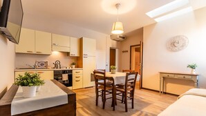A modern kitchen with wooden cabinets, a dining table with chairs, a small table with a plant, and a clock on the wall.