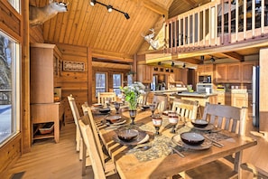 Interior de una cabaña de madera con mesa de comedor para cuatro, zona de cocina y un dormitorio en entrepiso.