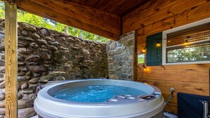 A hot tub in a wooden cabin with stone walls and a window with blinds.