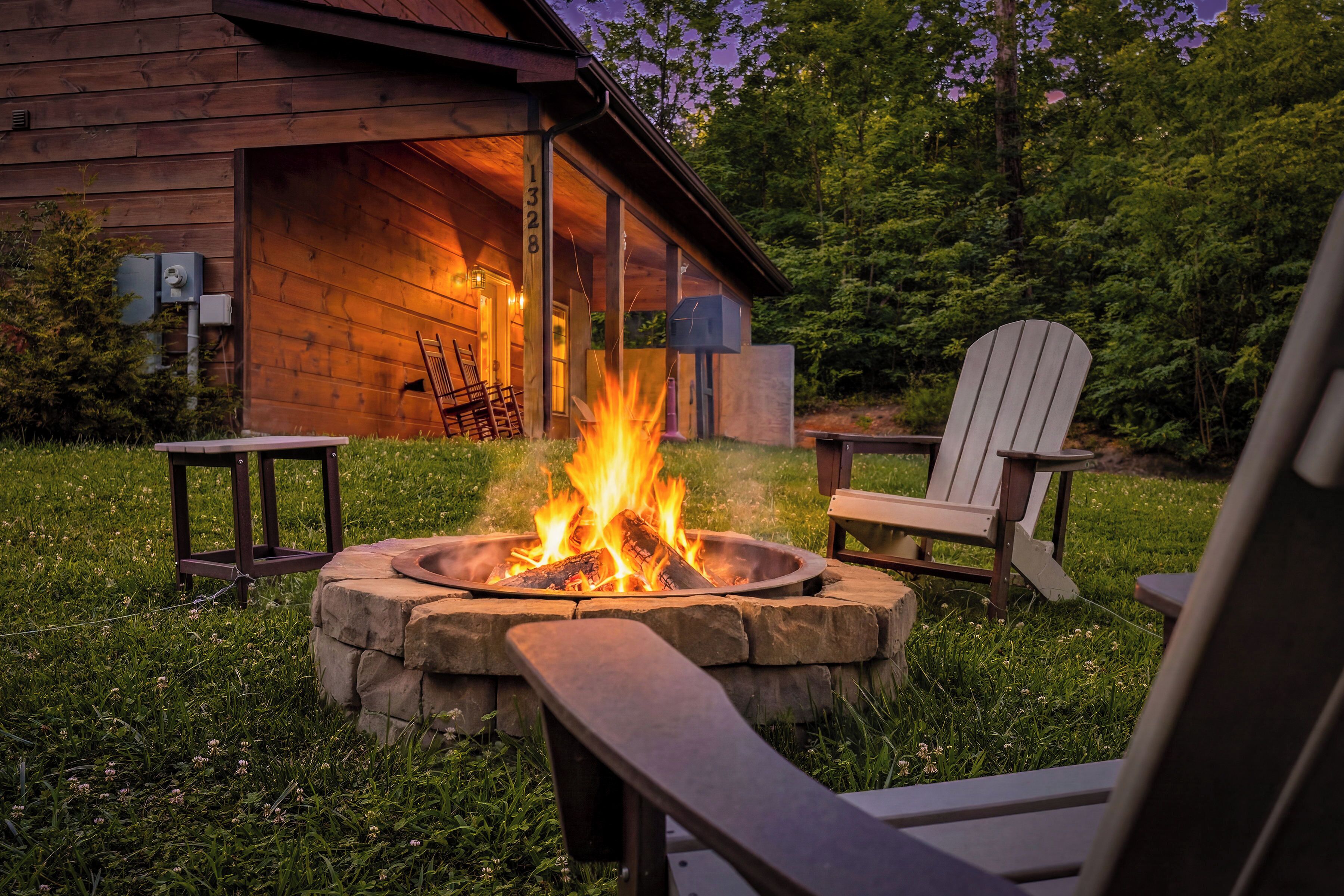 A wooden cabin with a fire pit in the center, surrounded by outdoor seating and a grassy area.