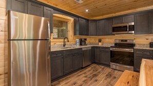 A modern kitchen with dark cabinets, stainless steel appliances, and a wooden floor.