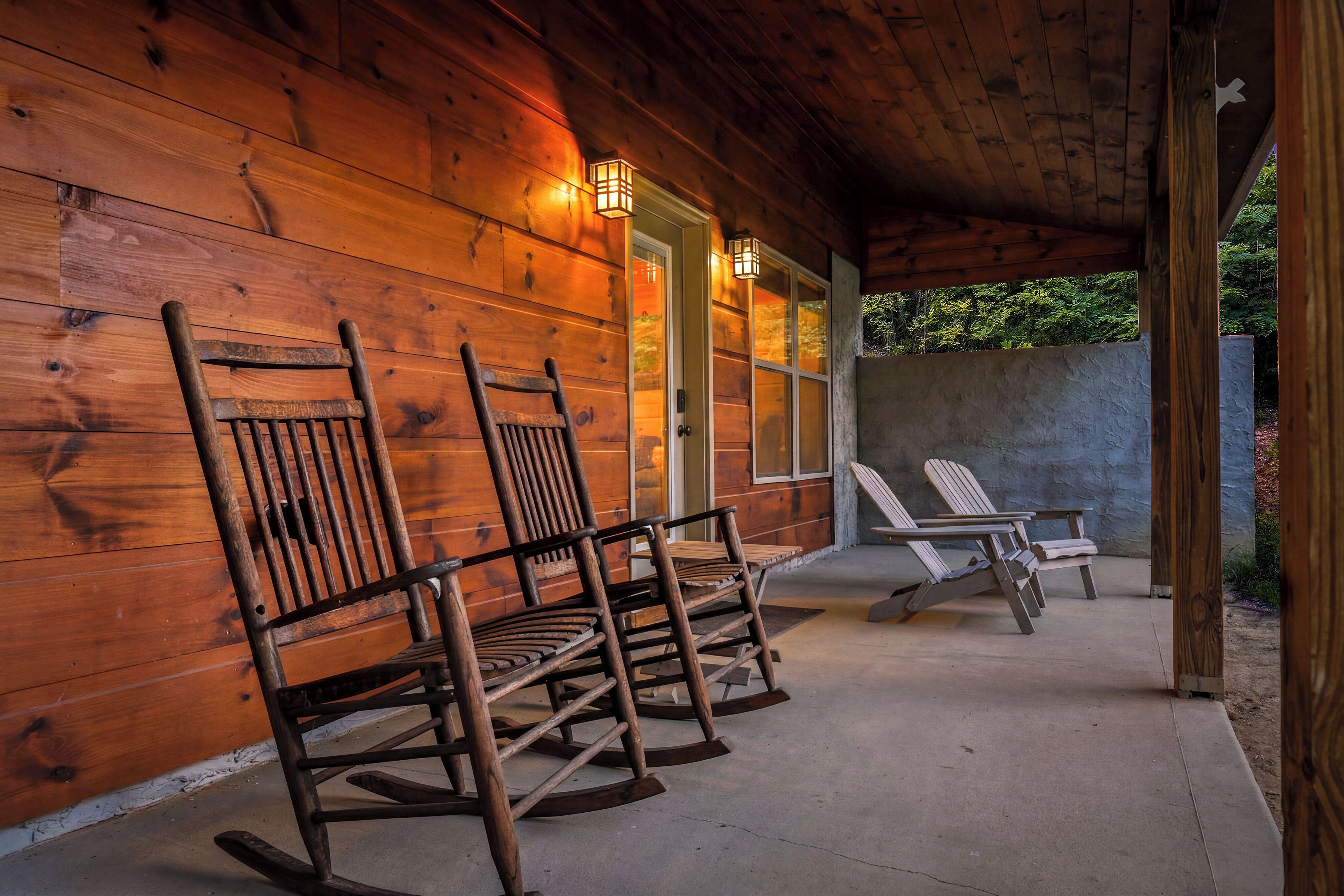 A wooden porch with rocking chairs and a table, a stone wall, and a wooden ceiling.