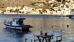 A boat docked near a waterfront with a backdrop of a hillside town. - SeaMe House I (Symi)