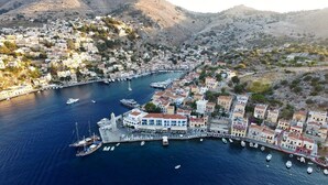 An aerial view of a coastal town with a marina, buildings, and hills in the background. - SeaMe House I (Symi)