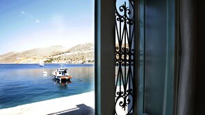 A coastal view through a door with a decorative metal frame, a boat on the water, and a sandy beach. - SeaMe House I (Symi)
