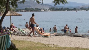 Ranta, jossa on aurinkotuoleja, olkikattoinen aurinkovarjo sekä ihmisiä uimassa ja rentoutumassa.