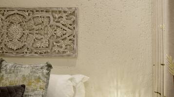 A neatly made bed with a decorative headboard, a bedside table with a lamp, and a wall-mounted air conditioner.