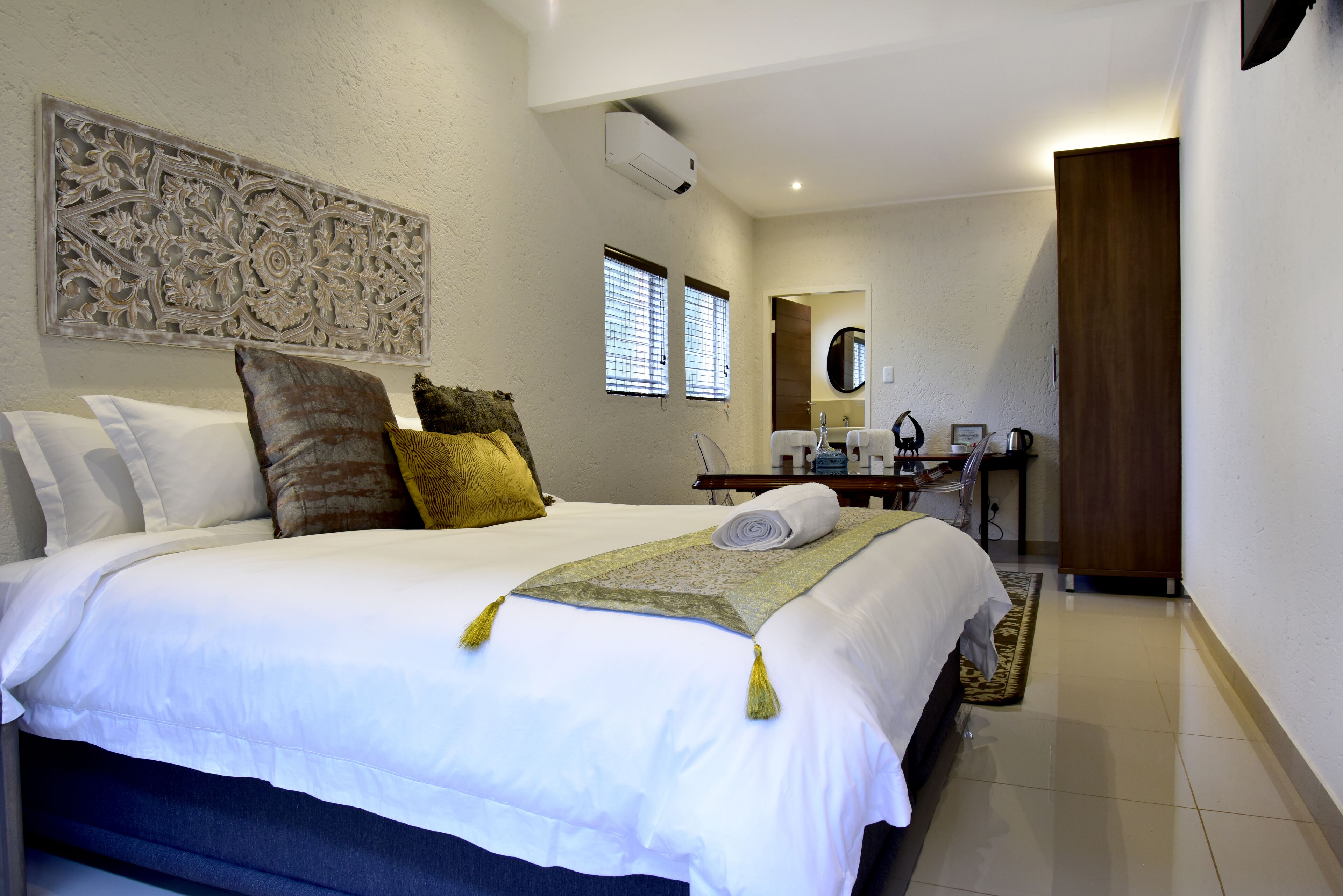 A neatly made bed with white linens, a decorative wall piece, and a wooden door.