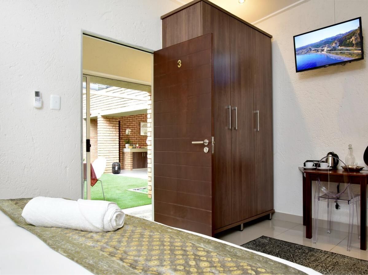 A hotel room with a bed, a wardrobe, a television, and a small table with a chair.