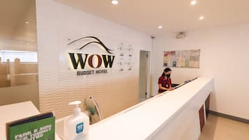 Modtagelsesdisk på WOW Budget Hotel med receptionist, en opslagstavle med meddelelser og skiltning for økoturismedestinationer.