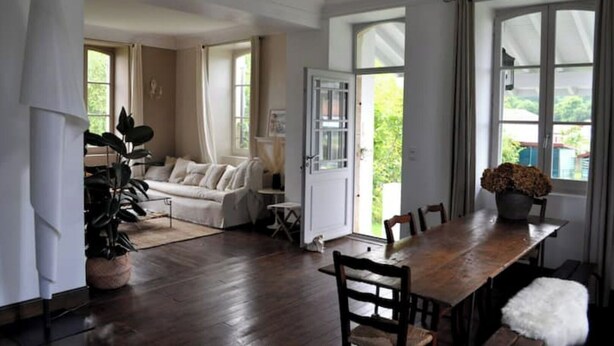 Ein geräumiges Zimmer mit großem Esstisch, einer Couch und Blick ins Freie durch eine Glastür.
