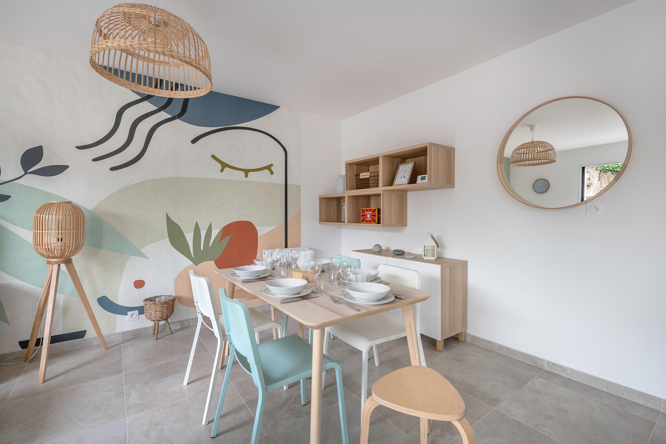 Un coin repas avec une table dressée pour quatre personnes, des chaises, une étagère fixée au mur et un luminaire suspendu.