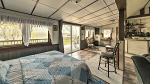 A bedroom with a large bed, a chair, a desk, and a view of the outdoors.