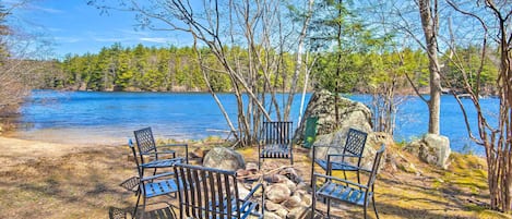 A lakeside seating area with metal chairs and a fire pit.