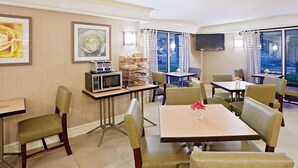 A hotel dining area with tables, chairs, a buffet station, and artwork on the walls.