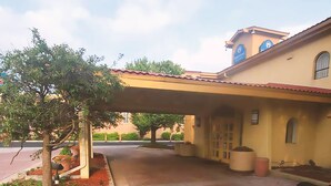 A building with a tiled entrance, a covered patio area, and a tree with potted plants.