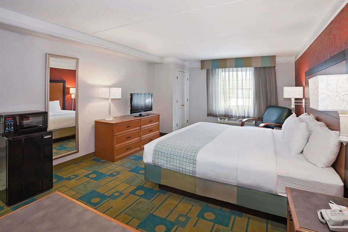Een hotelkamer met een bed, een televisie, een bureau met een computer, een spiegel en een raam met gordijnen.