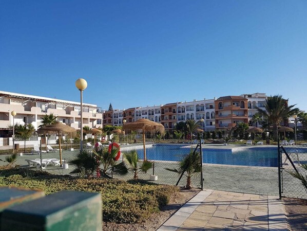 Een resort met een zwembad, palmbomen en een helderblauwe lucht.