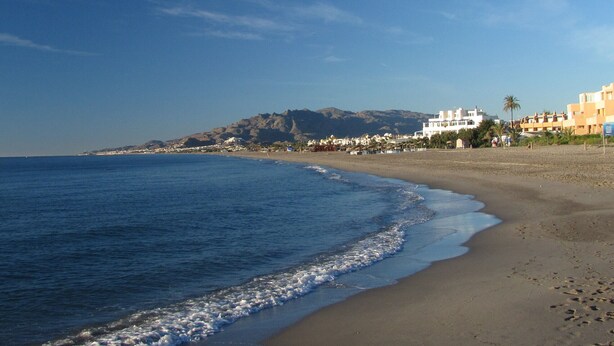A beach with a clear view of the ocean, a sandy shore, and buildings in the background. - Naturist Baja house with courtyard in first line! (Vera)