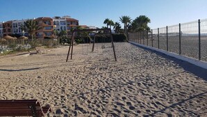 A sandy beach with a swing set and a fenced area, palm trees, and buildings in the background. - Naturist Baja house with courtyard in first line! (Vera)