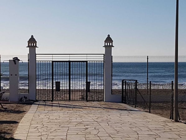 Ein gepflasterter Weg führt zu einem verschlossenen Eingang mit Blick auf das Meer.
