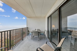 A balcony with a table and chairs, overlooking a beach.
