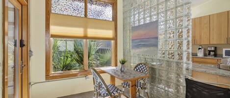 A compact kitchen with a dining area, featuring a window with blinds, a decorative glass partition, and wooden cabinets.
