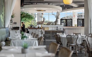 Un ristorante con tavoli rotondi, una zona bar e un'ampia scultura di cervo.