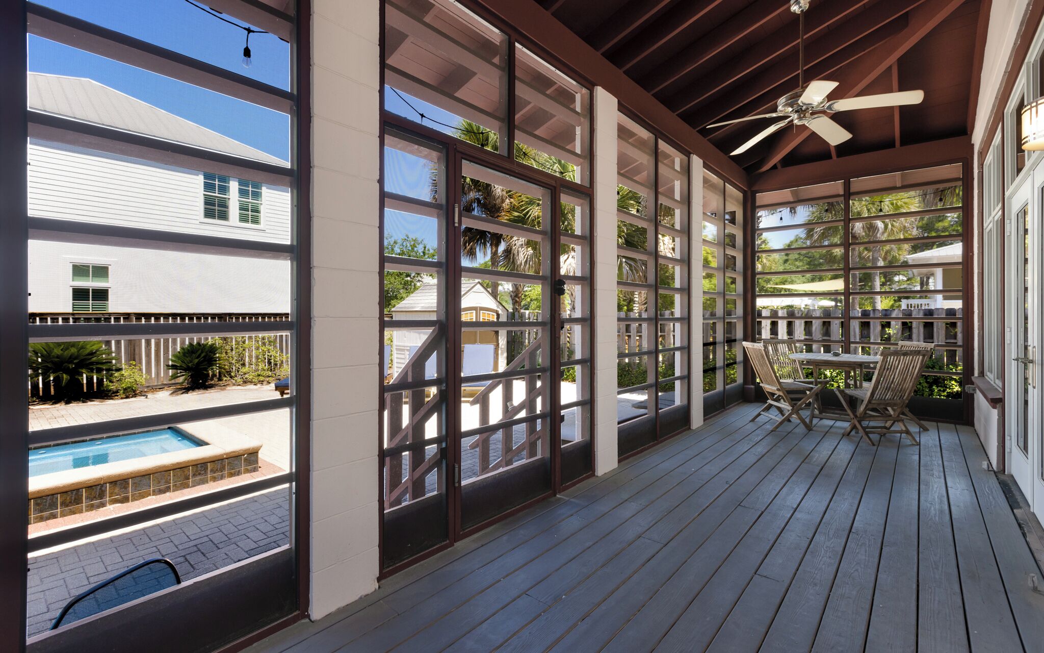 A covered outdoor area with a pool, wooden deck, and large windows.