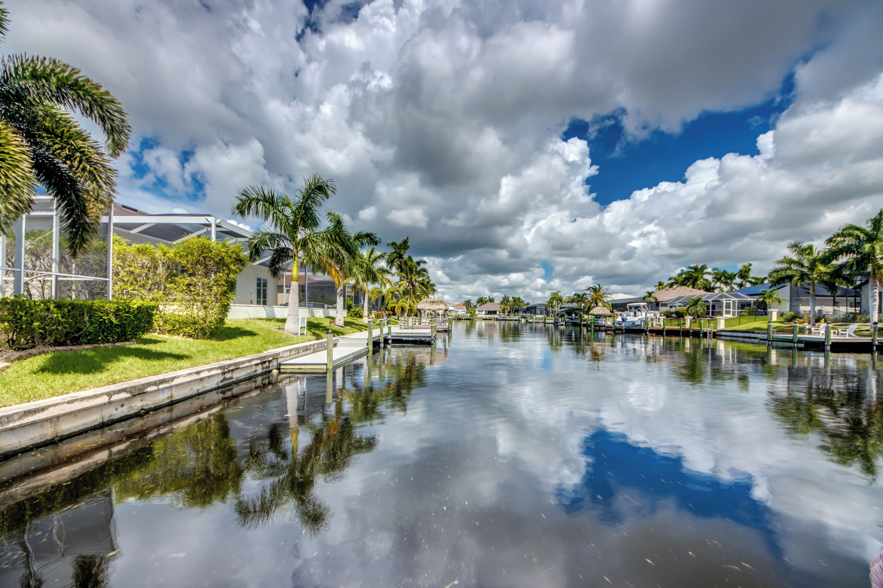 A calm waterway with a clear sky, palm trees, and modern buildings along the banks.