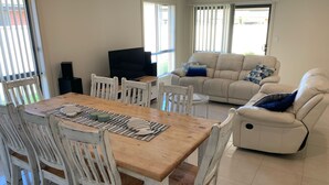 Ein Essbereich mit Holztisch und weißen Stühlen, einer Couch und einem Fernseher.