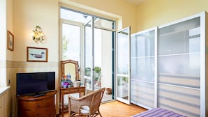 Quarto com cama, televisão, penteadeira, cadeira e varanda com vista.