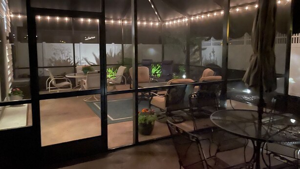 Een overdekt terras met sfeerverlichting, glazen wanden en een combinatie van stoelen en tafels.