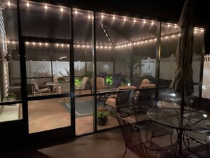Un área de estar al aire libre techada, con luces colgantes, divisiones de vidrio y una variedad de sillas y mesas.