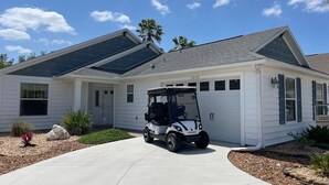 Een gelijkvloers huis met garage, een golfkarretje ervoor en een keurig onderhouden gazon.