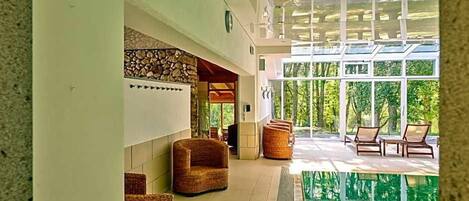 A modern indoor pool area with wicker furniture and a stone wall.