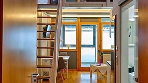 A spacious loft-style room with a wooden staircase leading to an upper level, a dining area with a table and chairs, and a view through large windows. - Aquaquell Bad Pilzweg Hotel & Spa (Fuerstenzell)