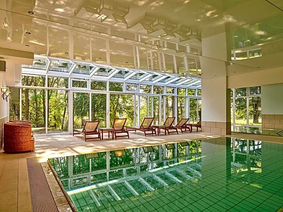 Una piscina interior con techo de cristal, sillones de descanso y vistas a zonas verdes.