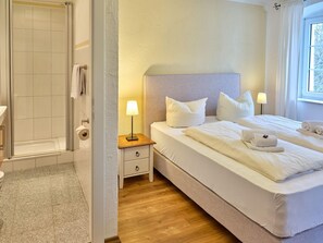 A hotel room with a shower, a bedside table with a lamp, a bed with pillows, and a window with curtains. - Aquaquell Bad Pilzweg Hotel & Spa (Fuerstenzell)