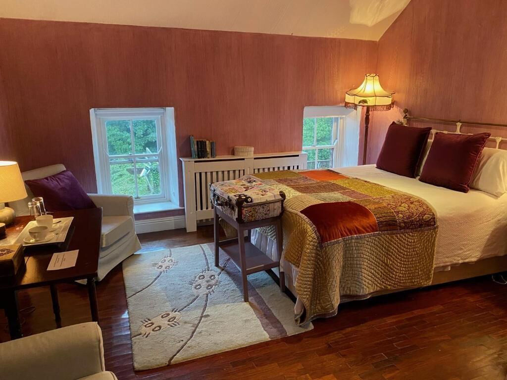 Un dormitorio con cama, mesita de noche, lámpara, silla y vistas al exterior a través de una ventana.