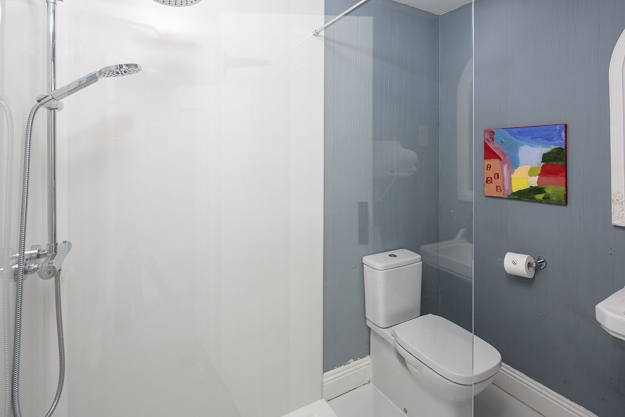 A bathroom with a shower, toilet, and a painting on the wall.