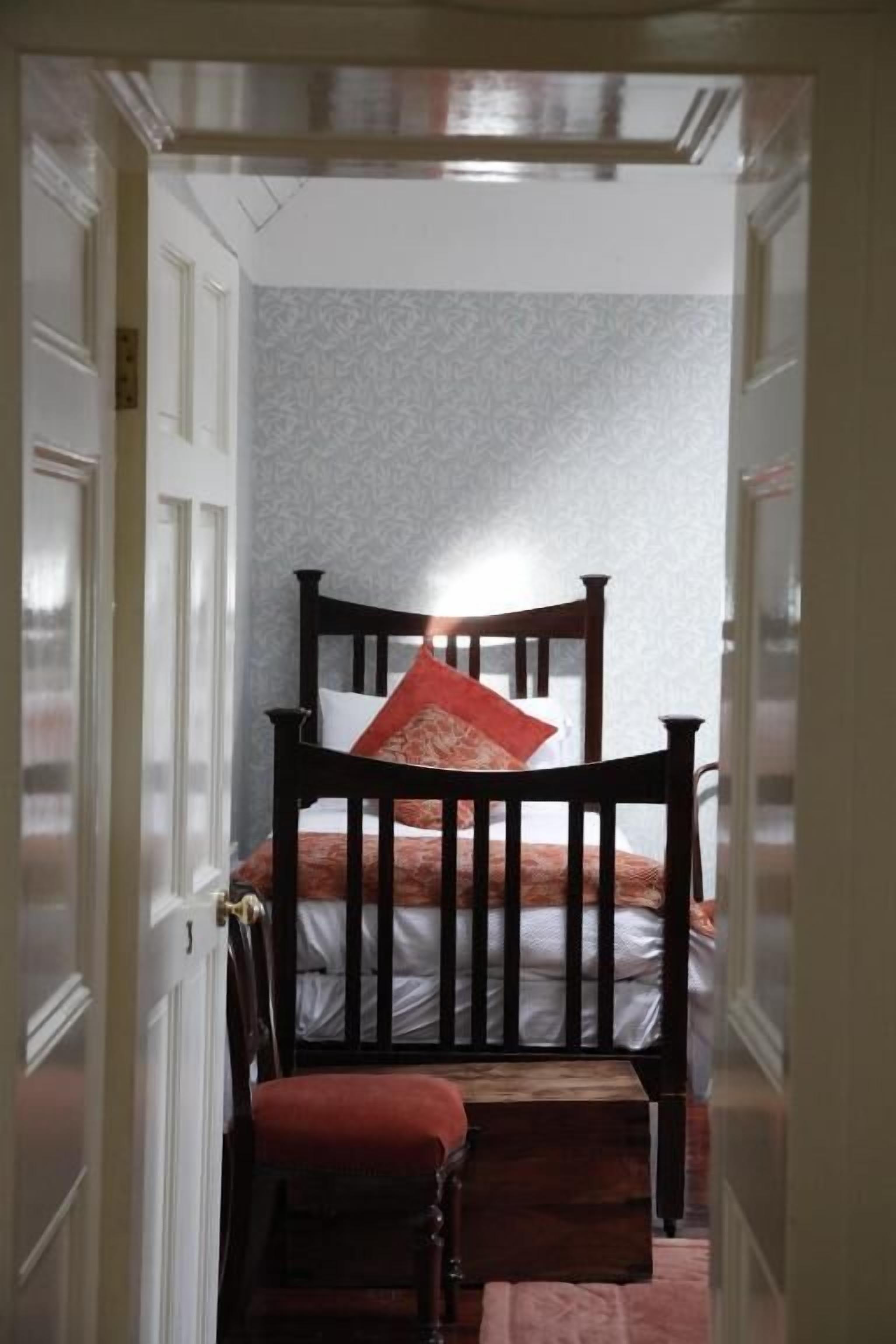 A narrow hallway leading to a bedroom with a bed, a chair, and a small table.