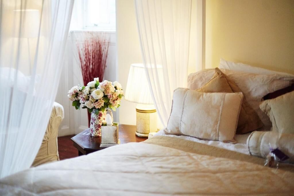 A neatly made bed with white linens, a bedside table with a lamp, and a vase of flowers.
