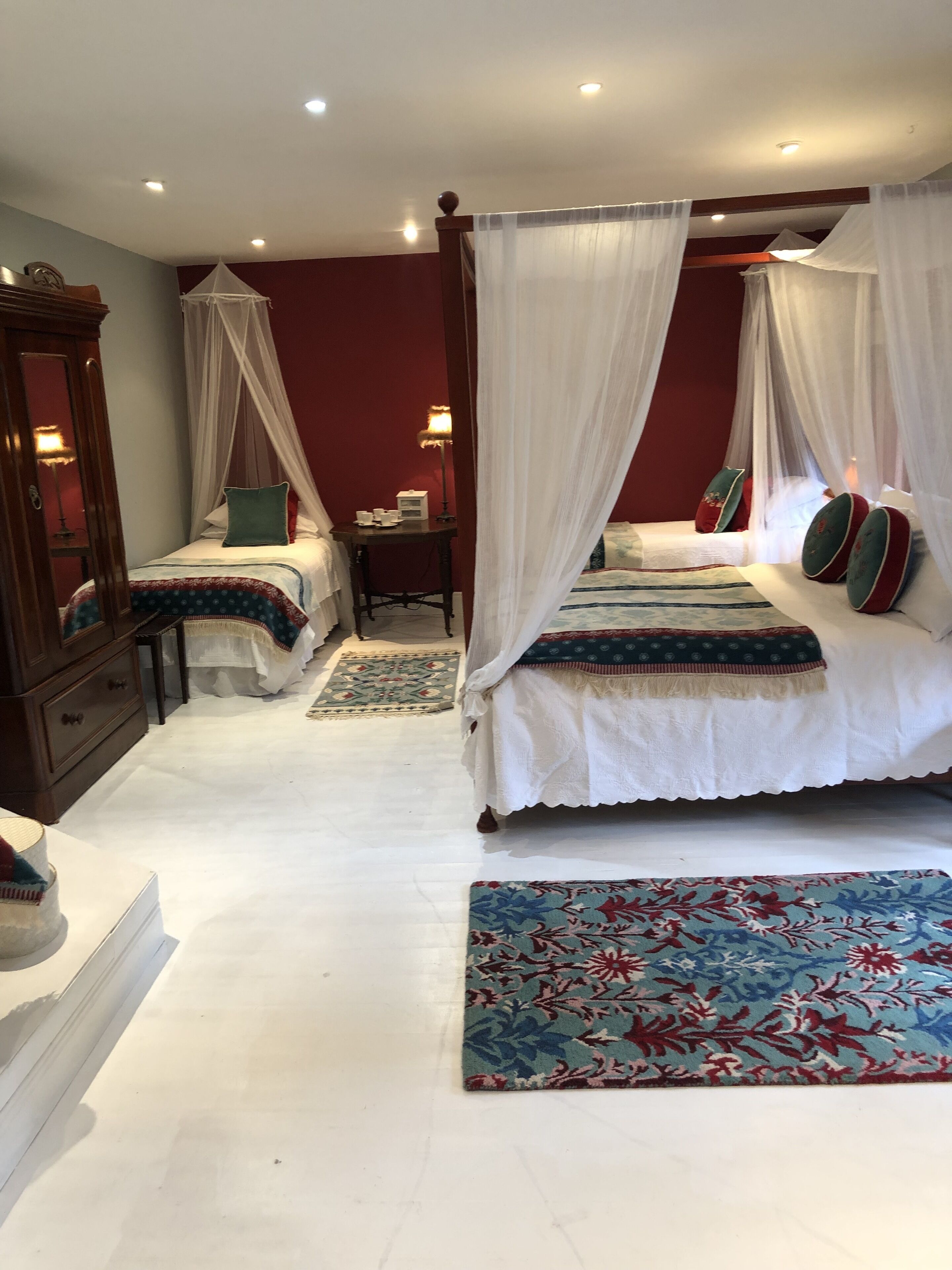 A bedroom with two beds, each with a canopy, a nightstand, a lamp, and a patterned rug.