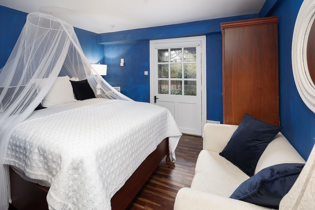 Un dormitorio con cama, dosel blanco, puerta de madera y sillón blanco.