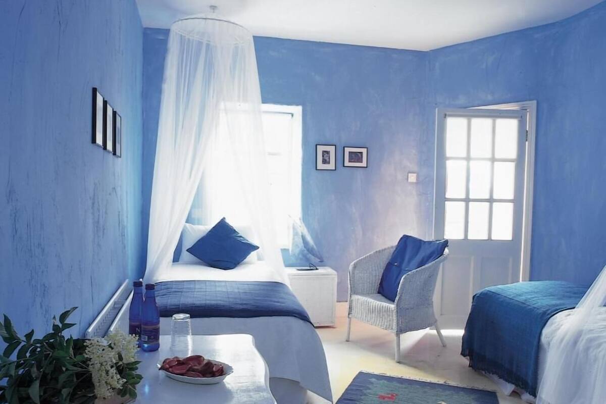 Un dormitorio con dos camas, una silla, una mesita de noche con una planta y un plato de comida, y una ventana con vistas.